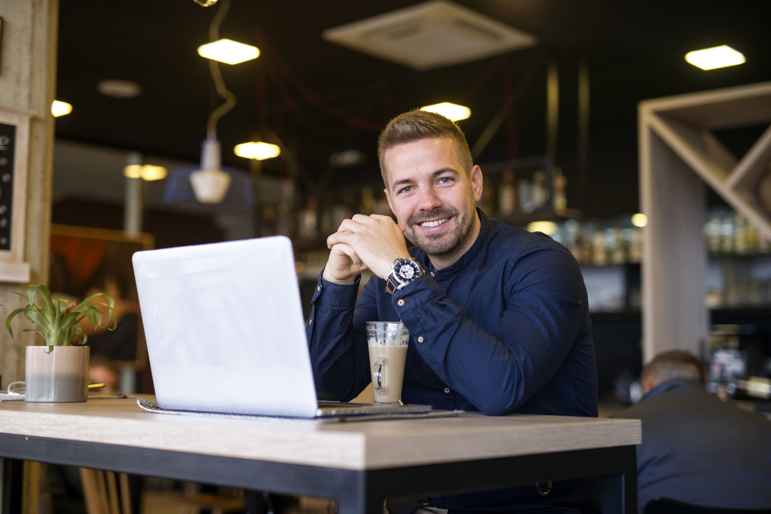 portrait-smiling-man-sitting-cafe-bar-with-his-laptop-computer-min