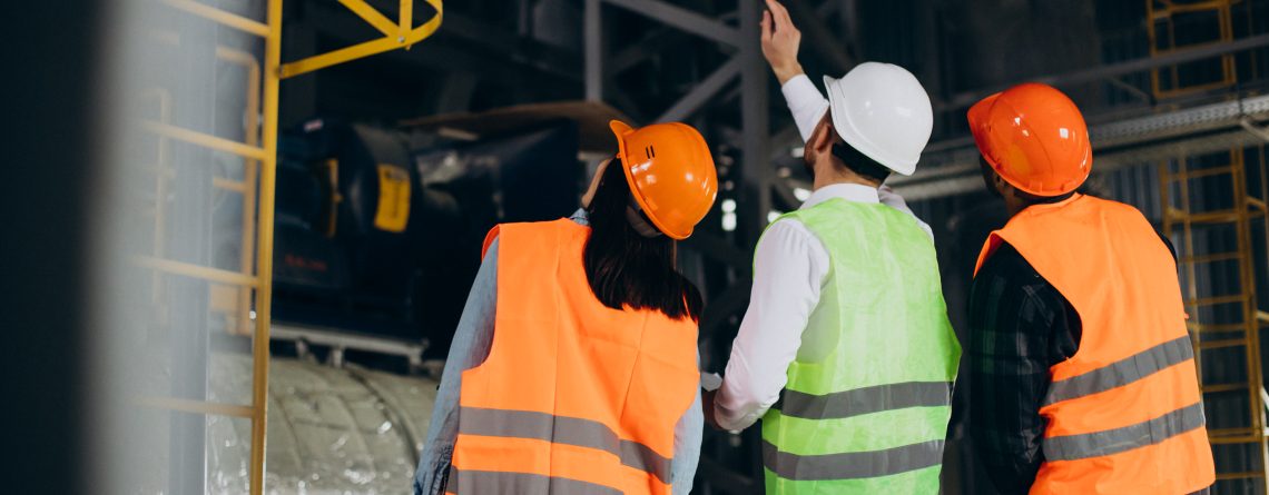 three-factory-workers-safety-hats-discussing-manufacture-plan-1140x445